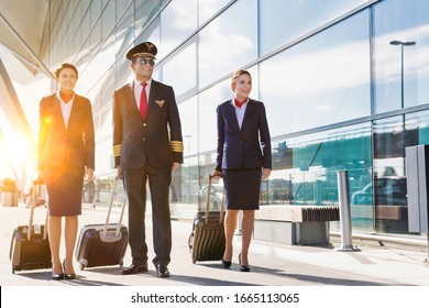 Mature pilot with young beautiful flight attendants walking in airport - Shutterstock ID 1665113065