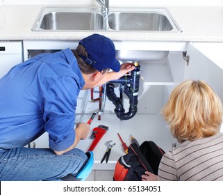 Mature Plumber Fixing A Sink At Kitchen