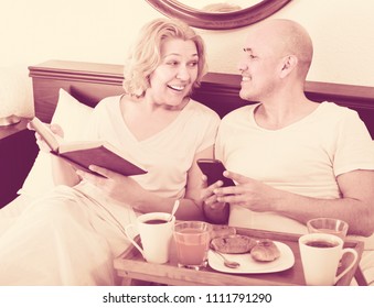 Mature positive couple reading book while having breakfast 
 - Powered by Shutterstock