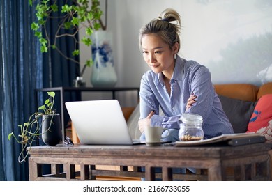 Mature Professional Asian Woman Working From Home Sitting In Couch Looking At Laptop Computer