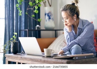 mature professional asian woman working from home sitting in couch looking at laptop computer