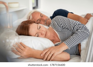 Mature relaxed woman dreaming and sleeping with her husband on bed at home. Senior man embracing beautiful asleep woman with eyes closed in the morning. Mature couple sleeping together in their bed. - Powered by Shutterstock