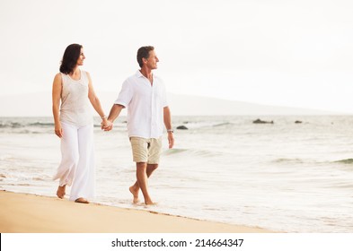 Mature Retired Couple Enjoying Sunset Walk On The Beach