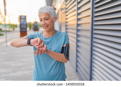 Mature Runner Checking Smart Watch. Checking Fitness Statistics On Smart Watch. Athletic mature woman monitoring her running performance on smartwatch - Powered by Shutterstock