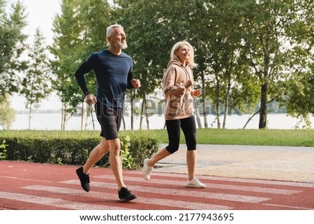 Mature runners couple athletes jogging together in the morning in stadium park. Slimming workout training outdoors.