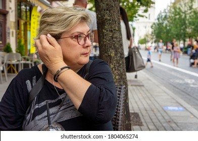 A Mature Sad Woman With Glasses Walks Through The Streets Of The Old City. Drinks A Cocktail At A Table In A Street Cafe And Looks Into The Distance.