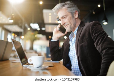 Mature Salesman Preparing Sales Pitch On Cellphone And Computer