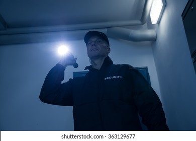 Mature Security Guard Searching With Flashlight In Office Building