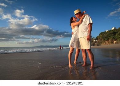 Mature Senior Adult Couple Kiss On Tropical Beach Standing In Ocean Water.