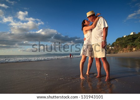 Mature senior adult couple kiss on tropical beach standing in ocean water.