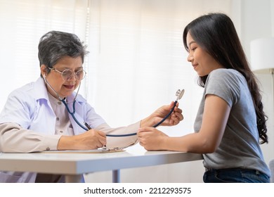 Mature, Senior Asian Physician, Psychiatrist, General Woman Doctor Consulting Concerned With Young Patient, Using Stethoscope To Listen, Appointment At Clinic, Hospital. Health Care, Check Up Medical.