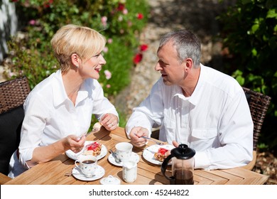 Mature or senior couple having coffee and strawberry cake on the porch in front of their home, it is summer and the roses look beautiful - Powered by Shutterstock