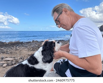 Mature senior man sitting at the beach cuddling his Cavalier King Charles dog. Best friend and love forever concept. Horizon over the water - Powered by Shutterstock