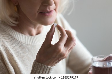Mature senior middle aged woman holding pill and glass of water taking painkiller to relieve pain, medicine supplements vitamins, antibiotic medication, meds for old person concept, close up view - Powered by Shutterstock