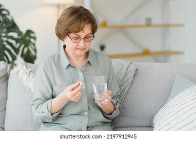 Mature senior middle aged woman holding pill and glass of water taking painkiller to relieve pain, medicine supplements vitamins, antibiotic medication, meds for old person concept, close up view - Shutterstock ID 2197912945