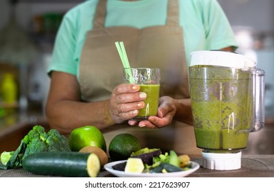 Mature Senior Woman Drinking Healthy Green Smoothie Holding A Glass With Straws. Smiling Caucasian Lady In Home Kitchen Drinking Detox Juice