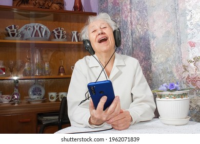 Mature Senior Woman In Headphones Singing A Song At Home. Positive And Happy Emotions Concept