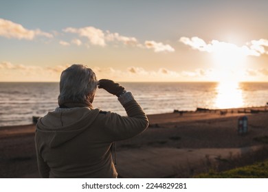 Mature senior woman shades her eyes as she looks across the sea towards the setting winter sun, a sense of closure, ending - Powered by Shutterstock