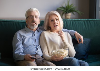 Mature Sensitive Sixty Years Old Couple Sitting On Couch Eating Pop-corn Watching Drama Movie Feels Amazement And Empathy, Emotional Husband And Wife Spends Lazy Weekend Time Together At Home Concept