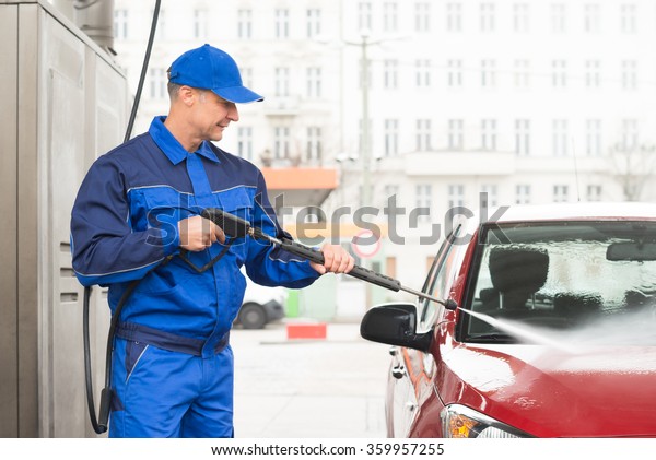 Mature serviceman with high pressure water jet
washing red car at service
station