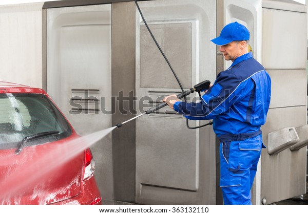 Mature serviceman with high pressure water jet\
washing red car at service\
station