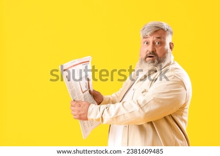Mature shocked man with newspaper on yellow background