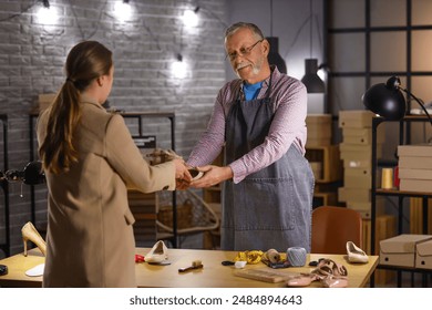 Mature shoemaker taking shoes from client in workshop - Powered by Shutterstock