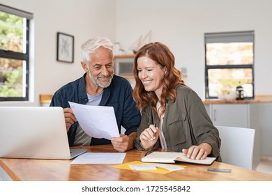 Mature smiling couple sitting and managing expenses at home. Happy senior man and mid woman paying bills and managing budget. Middle aged couple checking accountancy and bills while looking receipt.