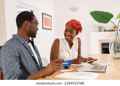 Mature Smiling Couple Sitting And Managing Expenses At Home. Happy Mid Black Man And Woman Paying Bills And Managing Budget. Middle Aged African American Couple Checking Accountancy And Bills.