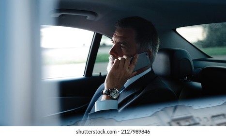 Mature smiling man talking over phone while sitting in taxi. Happy business man sitting on back seat of car using mobile phone to communicate. Businessman talking over cellphone while commuting.