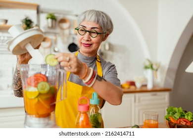 Mature Smiling Tattoo Woman Eating Salad, Fruits And Vegetables. Attractive Mature Woman With Fresh Green Fruit Salad At Home. Senior Woman Apron Standing In The Kitchen Counter Relaxing In House