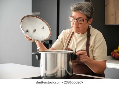 Mature Spanish woman opening a pressure cooker to cook cocido madrileño. - Powered by Shutterstock