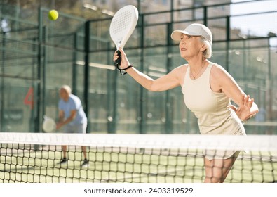 Mature sporty woman playing padel game in court on sunny day - Powered by Shutterstock