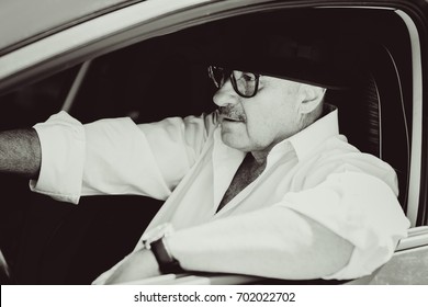 Mature Stylish European Or American Man Wear Black Hat, Glasses And White Shirt Driven Car, Modern And Hipster Style For Older People. Such A Good Mood At Pretty Day