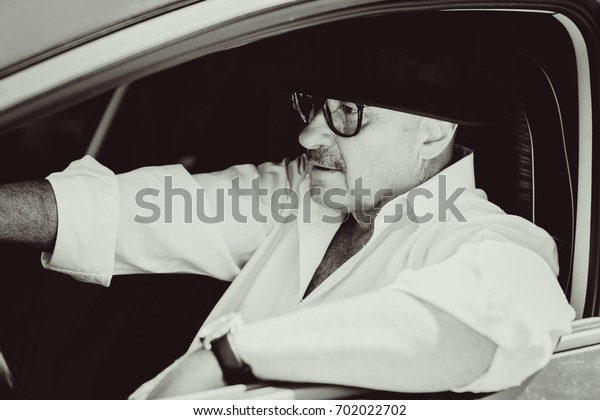 Mature stylish European or
American man wear black hat, glasses and white shirt driven car,
modern and hipster style for older people. Such a good mood at
pretty day