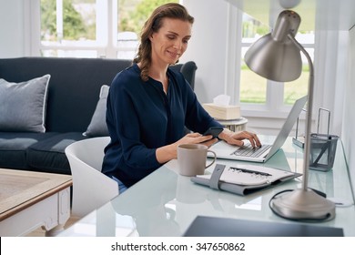 Mature Successful Business Woman Looking At Mobile Cell Phone While At Home In Office Work Space