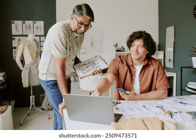 Mature tailor holding tablet with sketches while discussing new order with his designer - Powered by Shutterstock