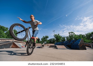 A mature tattooed urban man is performing tricks on a bmx bike while balancing on one wheel in a skate park. A middle-aged extreme man is practicing freestyle tricks on his bike. - Powered by Shutterstock