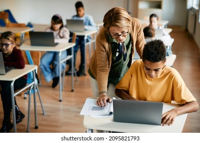 Mature teacher assisting to her elementary student in using laptop on computer class at school.