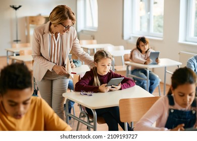 Mature teacher assisting her elementary student in using digital tablet during computer class at school. - Powered by Shutterstock