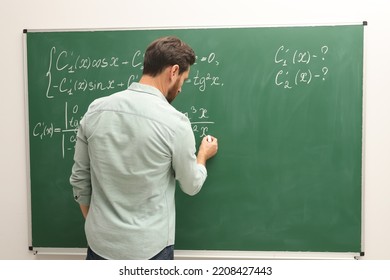 Mature Teacher Explaining Mathematics At Chalkboard In Classroom