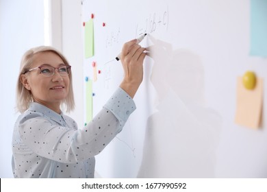 Mature teacher writing on whiteboard in modern classroom