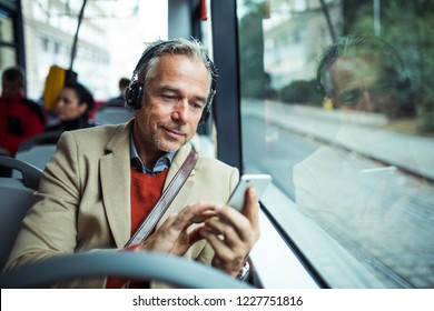 Mature tired businessman with heaphones and smartphone travelling by bus in city. - Powered by Shutterstock