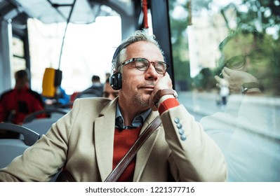 Mature tired businessman with heaphones travelling by bus in city. - Powered by Shutterstock