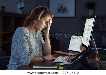 Mature and tired businesswoman working on computer until night. Portrait of a casual stressed lady with headache at desk. Exhausted business woman working late night at laptop in office.