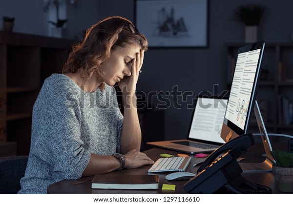 Mature and\
tired businesswoman working on computer until night. Portrait of a\
casual stressed lady with headache at desk. Exhausted business\
woman working late night at laptop in\
office.