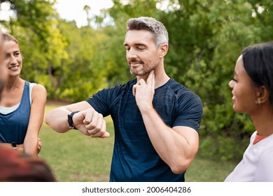 Mature tired man checking pulse after workout. Handsome middle aged man standing with group of friends measuring heart rate pulse on his neck and looking sport watch. Guy times the pulsations at park. - Shutterstock ID 2006404286