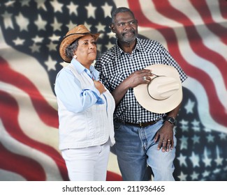 A mature western couple giving tribute to their country.  They're against a backdrop of a large American flag.