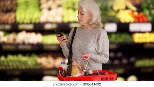 Mature White Lady In Produce Section Of Grocery Store Checking Smartphone