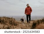 Mature white man walking dog on outdoor nature hill. Caucasianman in red down jacket walking with dog through nature hill. Middle aged Caucasian man travel with his dog in nature.